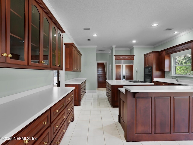 kitchen featuring a kitchen island, ornamental molding, built in appliances, light tile patterned floors, and a textured ceiling