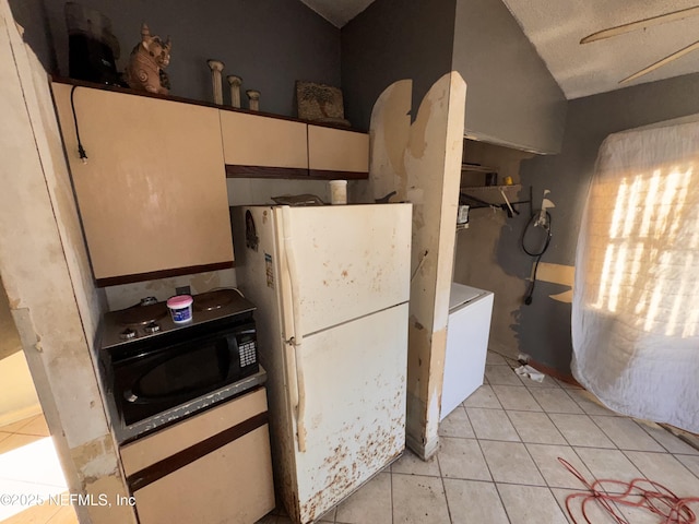 kitchen with white refrigerator, a textured ceiling, light tile patterned flooring, washer / clothes dryer, and vaulted ceiling