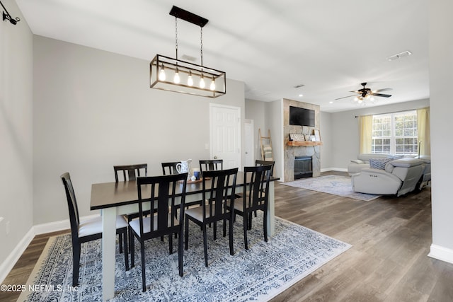 dining area with hardwood / wood-style flooring, ceiling fan, and a fireplace