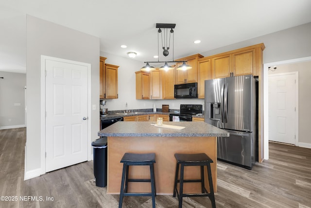 kitchen with a kitchen island, pendant lighting, a kitchen bar, hardwood / wood-style flooring, and black appliances