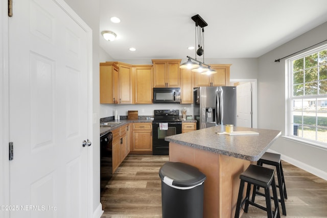 kitchen featuring decorative light fixtures, a wealth of natural light, black appliances, and a kitchen island