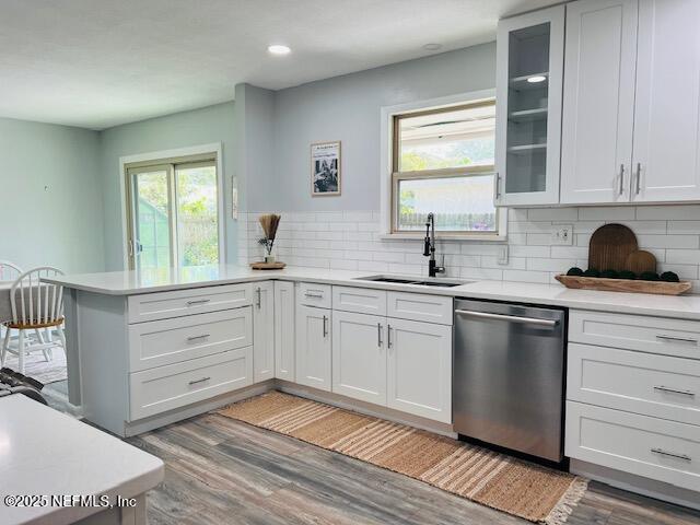 kitchen featuring a peninsula, a sink, light countertops, dishwasher, and light wood finished floors