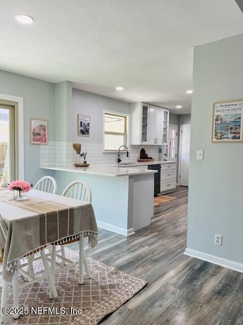 kitchen with decorative backsplash, glass insert cabinets, dark wood-type flooring, white cabinets, and a peninsula