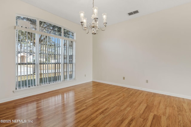 unfurnished room featuring an inviting chandelier, plenty of natural light, and hardwood / wood-style floors