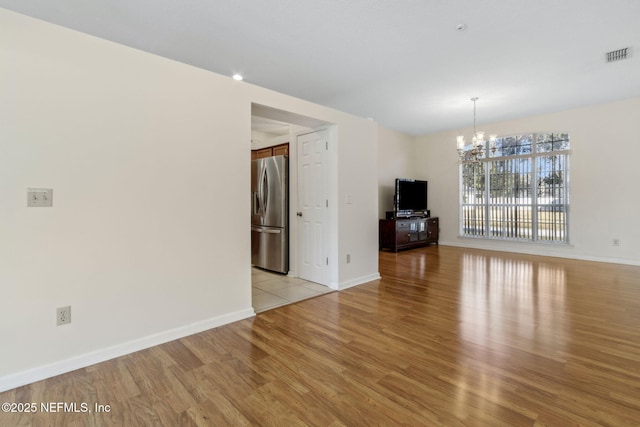 unfurnished living room with an inviting chandelier and light wood-type flooring