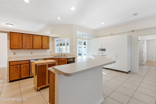 kitchen featuring sink, a center island, a textured ceiling, light tile patterned floors, and dishwasher