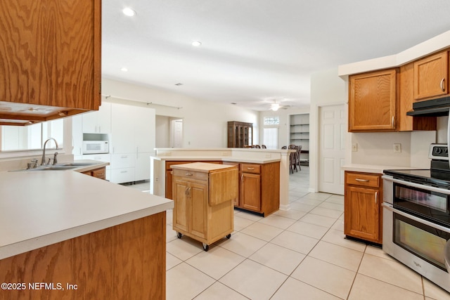 kitchen with light tile patterned floors, sink, double oven range, a center island, and kitchen peninsula