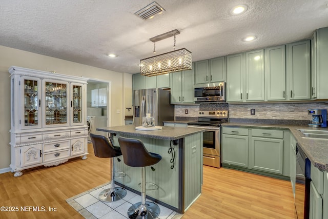 kitchen featuring green cabinetry, a textured ceiling, appliances with stainless steel finishes, pendant lighting, and backsplash