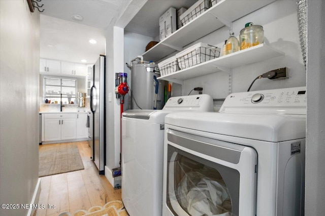 clothes washing area with independent washer and dryer, light hardwood / wood-style flooring, and water heater