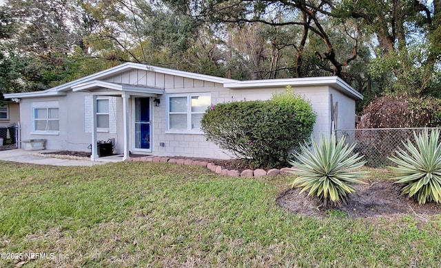 view of front of house featuring a front lawn, board and batten siding, concrete block siding, and fence