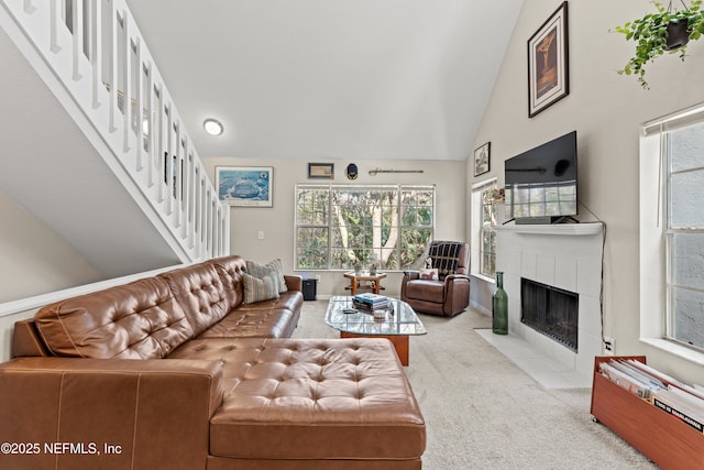 carpeted living room featuring high vaulted ceiling, a tile fireplace, and a healthy amount of sunlight