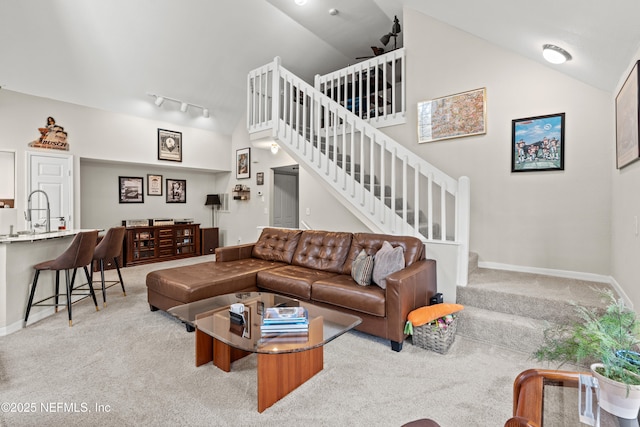 carpeted living room with high vaulted ceiling, rail lighting, and sink