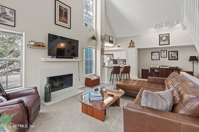 living room with light colored carpet, rail lighting, a tiled fireplace, and high vaulted ceiling