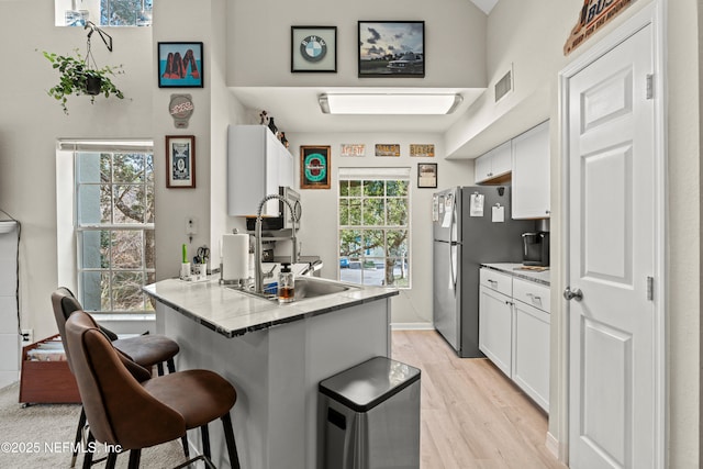 kitchen with a breakfast bar, sink, white cabinetry, kitchen peninsula, and light hardwood / wood-style floors