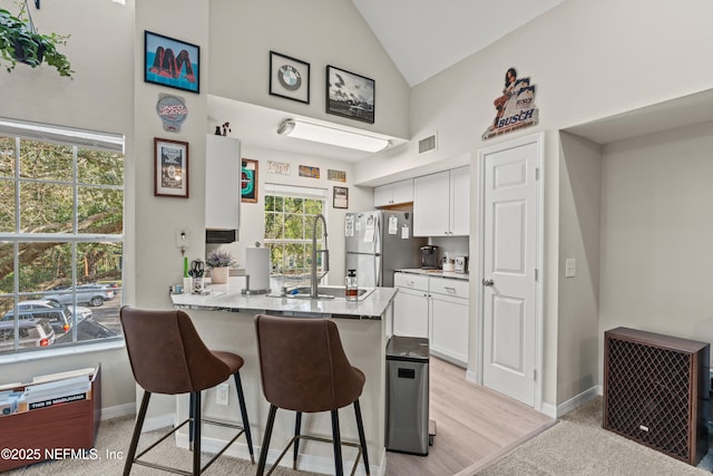 kitchen with sink, stainless steel fridge, a breakfast bar area, white cabinetry, and kitchen peninsula