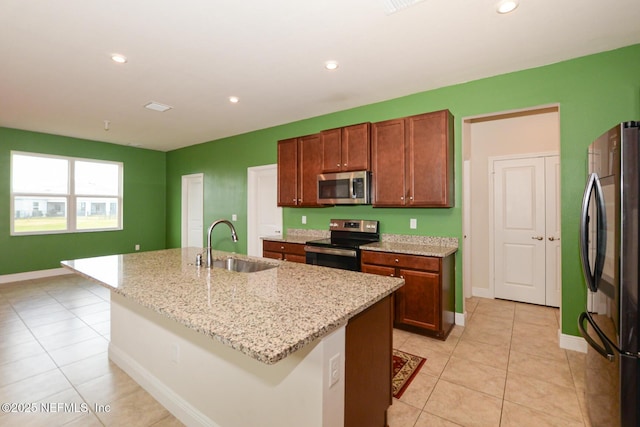 kitchen with light stone countertops, appliances with stainless steel finishes, sink, and a center island with sink