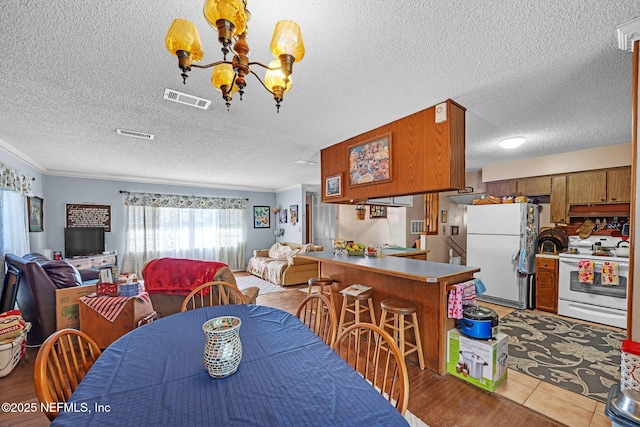 dining area with a notable chandelier, crown molding, a textured ceiling, and light wood-type flooring