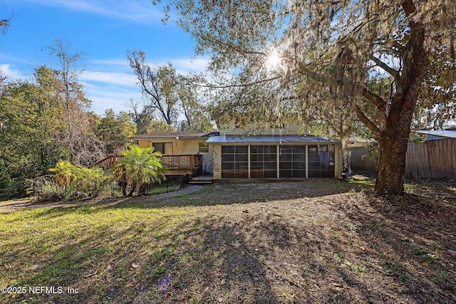 rear view of property with a wooden deck, a lawn, and a sunroom