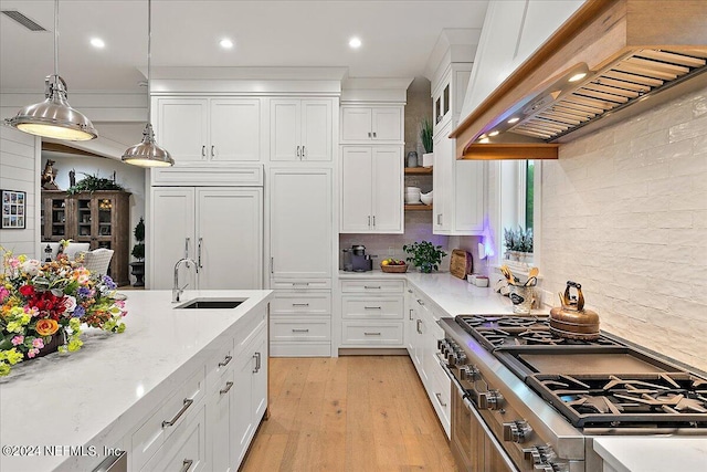 kitchen with sink, white cabinetry, paneled fridge, custom range hood, and decorative light fixtures