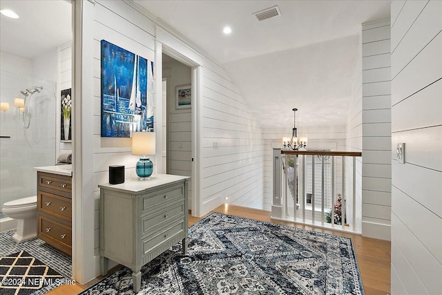 hallway with an inviting chandelier, lofted ceiling, wooden walls, and light wood-type flooring