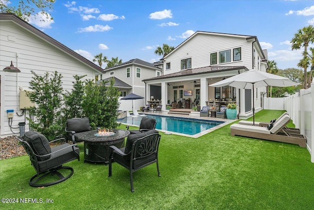 rear view of house with a yard, ceiling fan, an outdoor fire pit, a fenced in pool, and a patio area