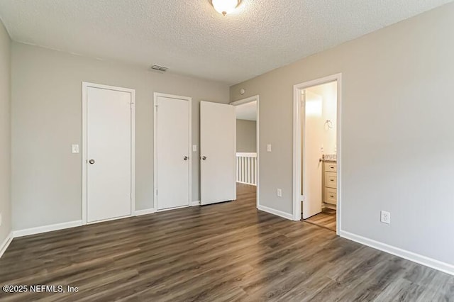 unfurnished bedroom featuring dark hardwood / wood-style floors, a textured ceiling, and ensuite bath