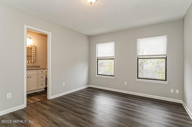 unfurnished bedroom with a textured ceiling, dark hardwood / wood-style flooring, and ensuite bath