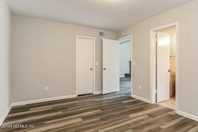 unfurnished bedroom featuring ensuite bathroom, dark wood-type flooring, and a textured ceiling