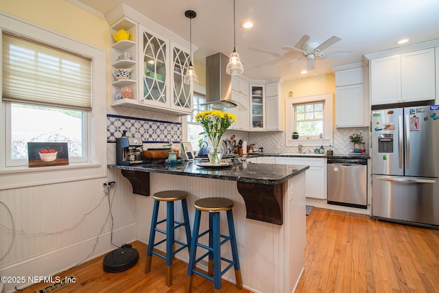 kitchen featuring a breakfast bar, appliances with stainless steel finishes, white cabinetry, hanging light fixtures, and island range hood