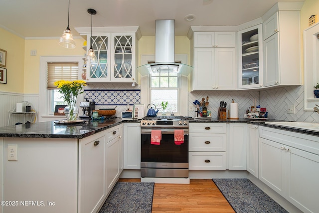 kitchen featuring white cabinetry, hanging light fixtures, gas stove, wall chimney range hood, and light wood-type flooring