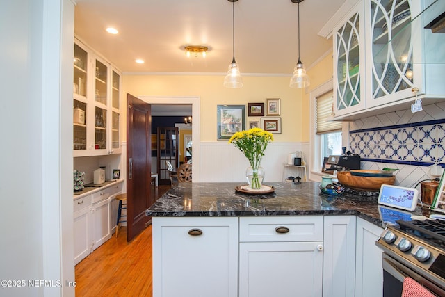 kitchen with white cabinetry, dark stone countertops, hanging light fixtures, crown molding, and light wood-type flooring