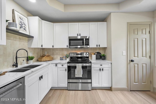 kitchen with appliances with stainless steel finishes, sink, white cabinets, light stone counters, and light hardwood / wood-style floors