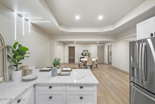 kitchen with white cabinets, light stone counters, stainless steel fridge with ice dispenser, a raised ceiling, and light wood-type flooring