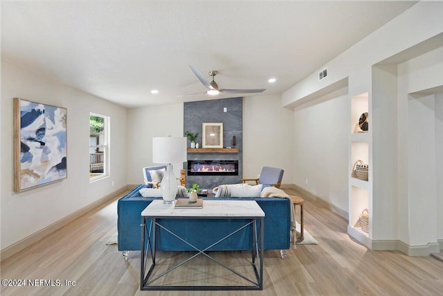 living room featuring ceiling fan, a fireplace, and light wood-type flooring