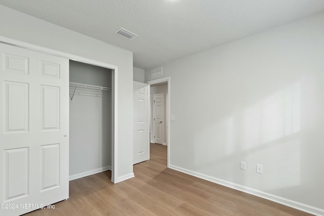 unfurnished bedroom featuring a textured ceiling, light hardwood / wood-style floors, and a closet