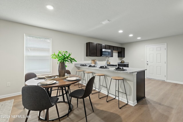 kitchen with a breakfast bar, a textured ceiling, kitchen peninsula, light stone countertops, and light hardwood / wood-style floors