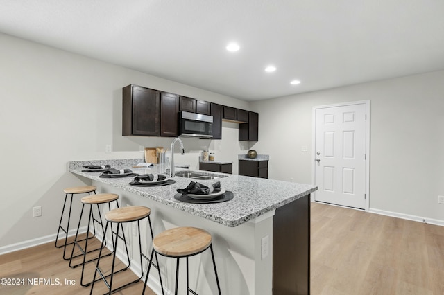 kitchen with sink, a breakfast bar area, kitchen peninsula, dark brown cabinets, and light hardwood / wood-style flooring