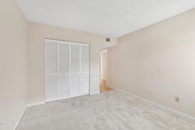 unfurnished bedroom with light carpet, a textured ceiling, and a closet