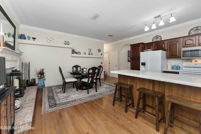 kitchen featuring dark brown cabinetry, a breakfast bar area, crown molding, white appliances, and light hardwood / wood-style floors