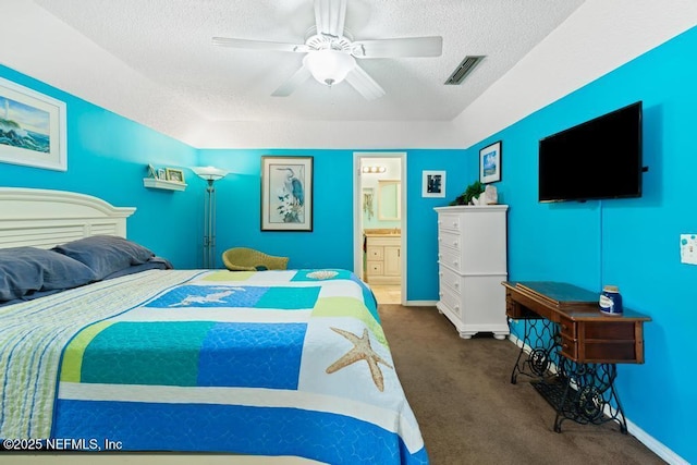 bedroom with ceiling fan, ensuite bath, a textured ceiling, and dark colored carpet