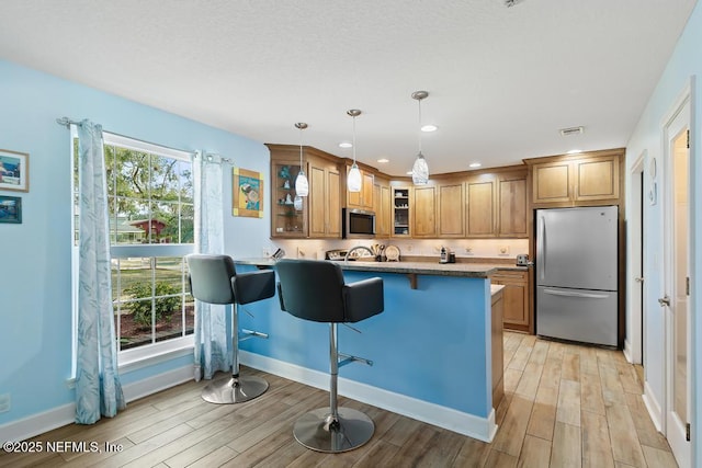 kitchen with appliances with stainless steel finishes, a breakfast bar area, light hardwood / wood-style floors, and decorative light fixtures