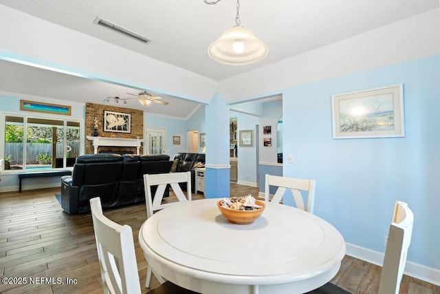 dining space with vaulted ceiling, ceiling fan, a fireplace, and hardwood / wood-style floors