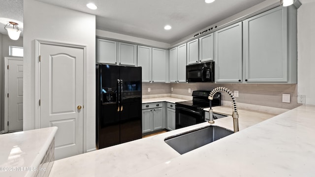 kitchen featuring sink, gray cabinetry, light stone countertops, decorative backsplash, and black appliances