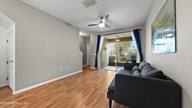 living room featuring hardwood / wood-style flooring, ceiling fan, and a textured ceiling