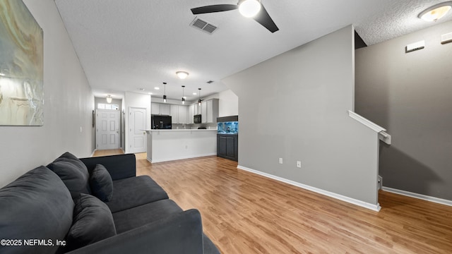 living room featuring ceiling fan, light hardwood / wood-style floors, and a textured ceiling