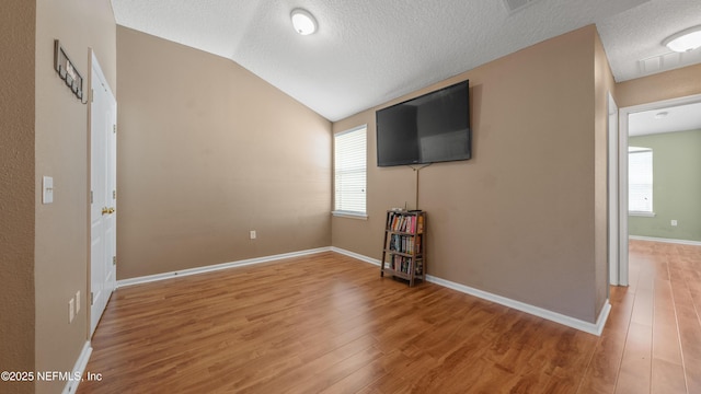 unfurnished living room featuring vaulted ceiling, a textured ceiling, and light hardwood / wood-style flooring