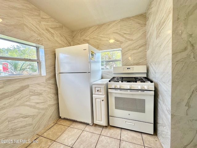 kitchen with light tile patterned flooring, white appliances, plenty of natural light, and tile walls