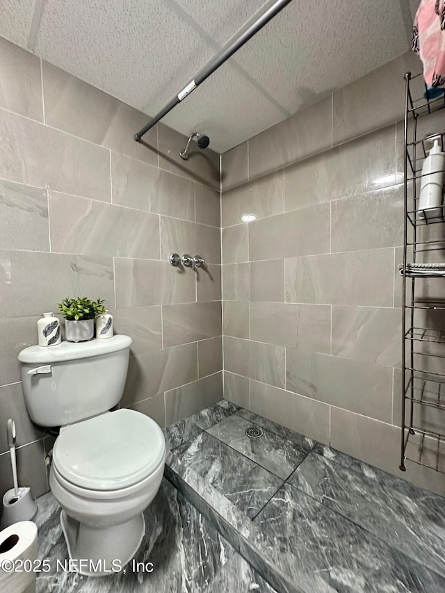 bathroom featuring tiled shower, toilet, and tile walls