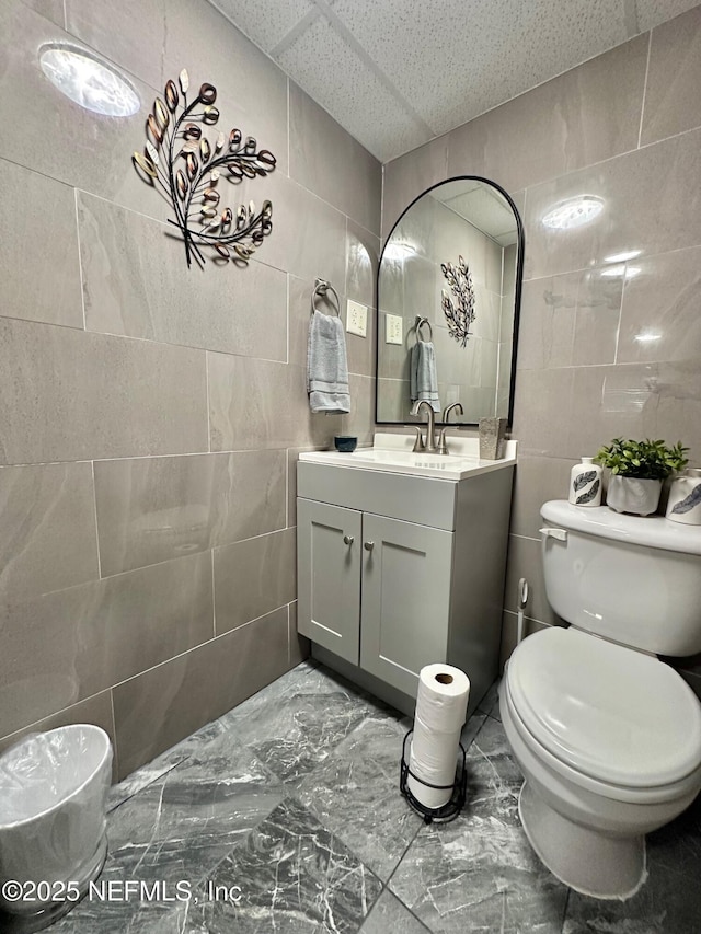 bathroom with vanity, toilet, and tile walls