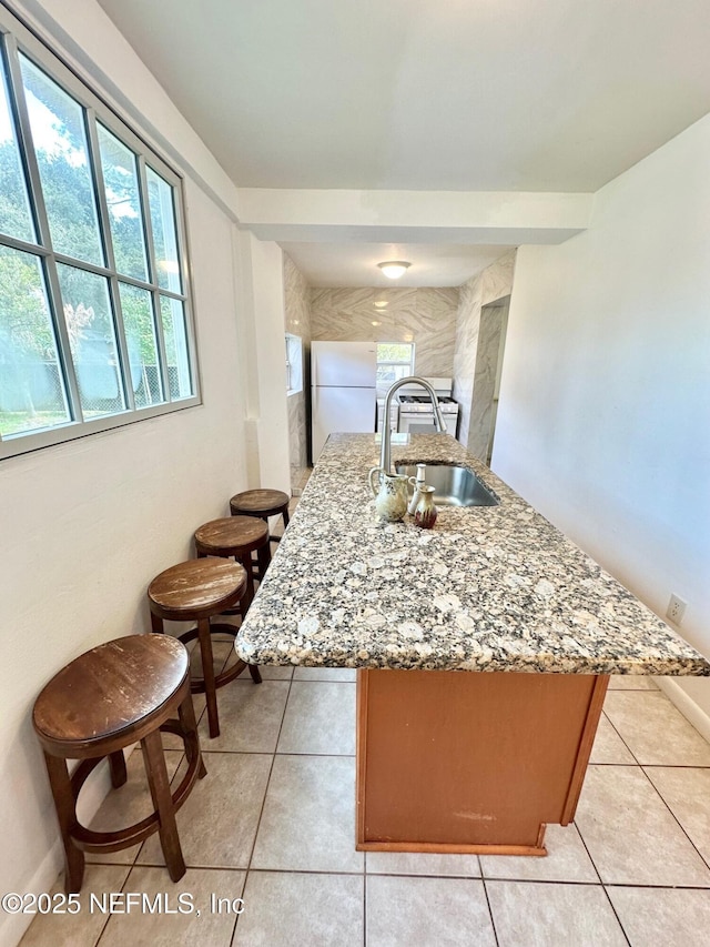 kitchen with sink, white fridge, a kitchen island with sink, light tile patterned floors, and light stone counters